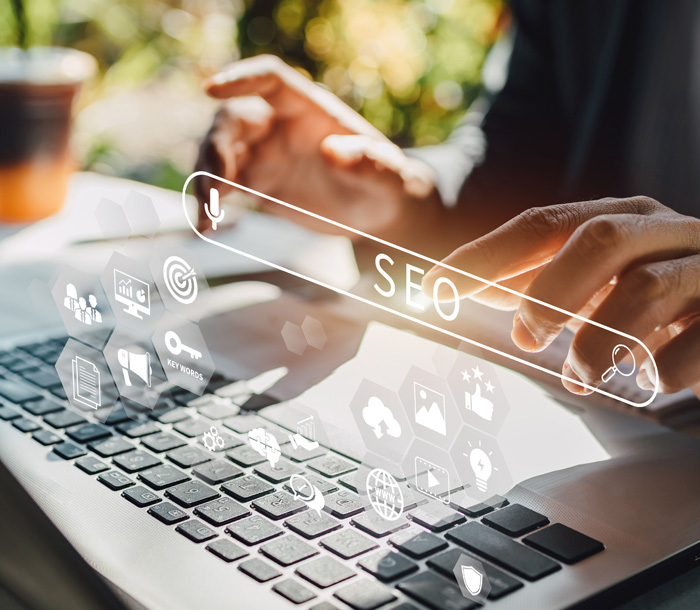 Hands typing on laptop with SEO icons