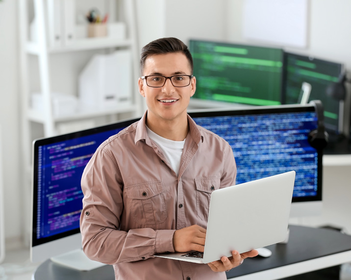 Man with laptop in front of computer screens.