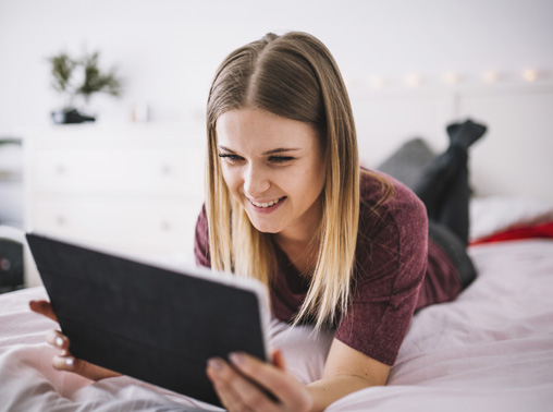 Young woman lying on bed with tablet.