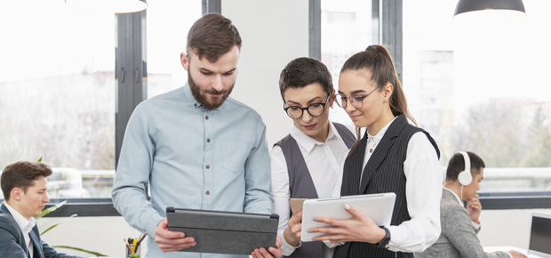 Three colleagues reviewing tablets in an office.
