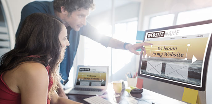 Man pointing at computer screen with a woman looking on.